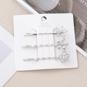 Détails de trois barrettes fleurs argentées avec cristaux sur carte de présentation blanche