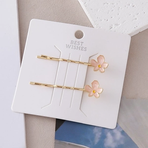 Barrettes dorées avec fleurs en émail rose sur une carte de présentation blanche élégante