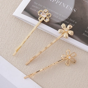 Détail de trois barrettes dorées en forme de fleur avec cristaux sur fond de magazine