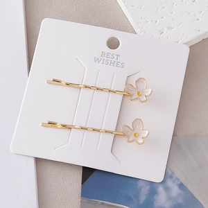 Détail de deux barrettes dorées à fleurs blanches sur une carte de décoration
