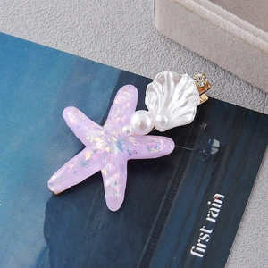 Detailed close-up of shell and starfish hair clip with pearls on a blue magazine