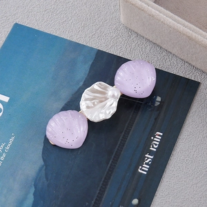 Detail view of shell hair clip with faux pearl and purple glitter accents on alloy base