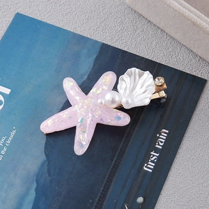 Macro detail of starfish and shell hair clip with pearls on a navy blue magazine