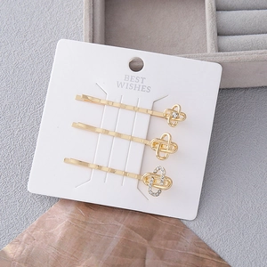 Set di 3 eleganti fermagli per capelli dorati con nodi geometrici e strass su carta bianca