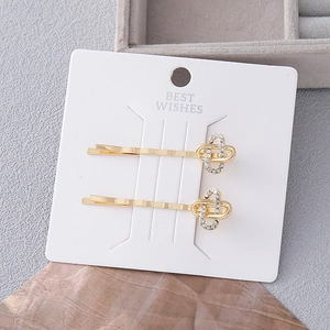 Eleganti fermagli per capelli dorati con strass e perle su cartoncino bianco