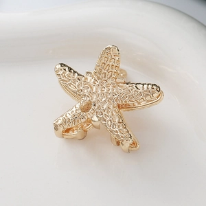 Elegant golden starfish hair claw clip with textured alloy finish on white ceramic