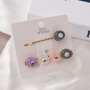 Détail de deux barrettes dorées avec des perles en résine colorées et de petits strass fins