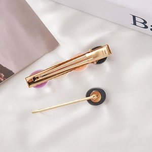Détail de barrettes dorées avec perles en résine colorées sur fond de tissu blanc