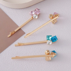 Detail of four golden bobby pins with colorful square crystals on white textured backdrop