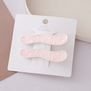 Détail de barrettes à cheveux ondulées roses avec perles blanches sur carte