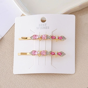 Détail de deux pinces à cheveux dorées avec cristaux roses et strass en forme de fleur et papillon