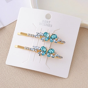 Détail de deux pinces à cheveux papillon en cristal bleu sur carte cadeau blanche