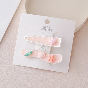 Détail de barrettes roses avec charms étoile de mer et coquillages sur support blanc