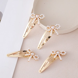 Set of 4 gold metal hair clips with faux pearl bow designs on a textured cream backdrop