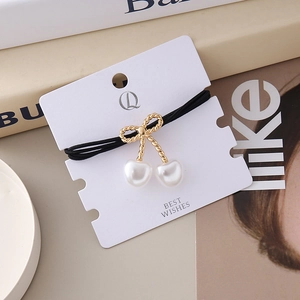 Élastique cheveux cerise élégant avec nœud doré et perles blanches sur carte support