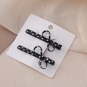 Elegant pair of polka dot bow hair clips on white card over soft beige fabric background