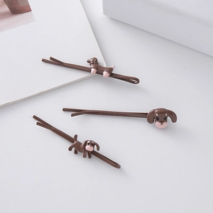 Close-up of three brown metal hair clips with cute cartoon dachshund dog motifs on a desk