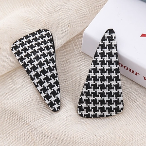 Close-up of black and white houndstooth tweed triangle hair clips on beige linen background