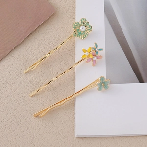 Dettaglio di tre fermagli per capelli a fiore dorati con petali in smalto e perle