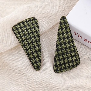 Close-up of green houndstooth pattern fabric hair clips on a soft beige linen background