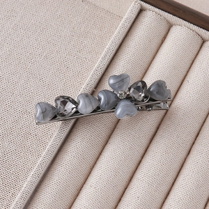 Detail view of heart shaped floral hair clip with marble and crystal stones on beige linen