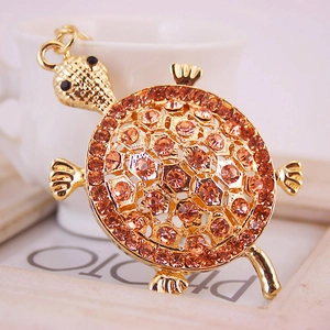 Porte-clés tortue dorée avec strass orange placé près d'une tasse en céramique