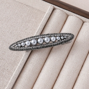 Detail of elegant oval hair clip featuring grey pearls and dark rhinestones on a metal base