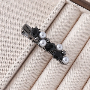 Detailed view of elegant black gemstone and pearl hair clip on beige velvet tray