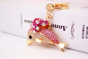 Macro detail of pink rhinestone dolphin keychain with bow charm on a golden alloy base