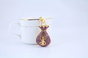 Macro detail of gold-plated money bag keychain with purple rhinestones and dollar sign
