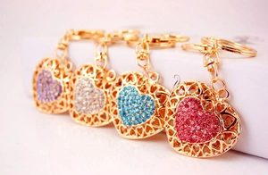 Detail of four colorful rhinestone heart keychains in purple white blue and pink with gold clasps