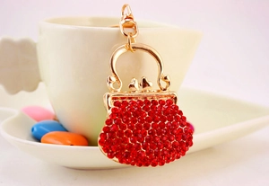 Detail of red rhinestone mini handbag keychain with gold metal clasp on a ceramic cup