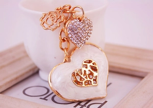 Detail of golden heart keychain with white enamel, rhinestones and rose charm pendant