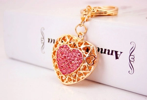 Detail of a golden heart keychain with pink rhinestones and hollow floral patterns