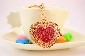 Detail of a sparkling heart keychain with pink rhinestones hanging on a white ceramic cup