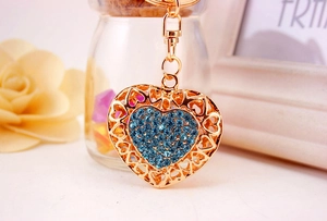 Detail of a golden heart keychain with blue rhinestones next to dried flowers