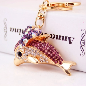 Sparkling dolphin keychain with purple rhinestones and golden bow on a white book