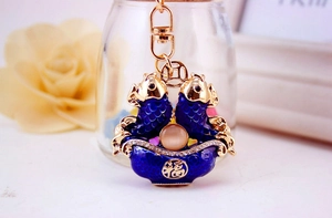 Macro detail of golden fish keychain with blue enamel, cat eye stone and Fu character
