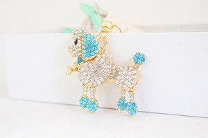 Détail macro du porte-clés caniche avec strass blancs et bleu ciel sur alliage doré