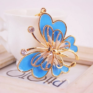 Sparkling blue butterfly keychain with gold plating and clear rhinestones on a white cup
