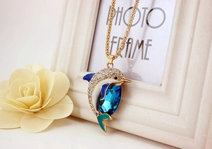 Detail of dolphin pendant with blue teardrop crystal and gold chain on frame