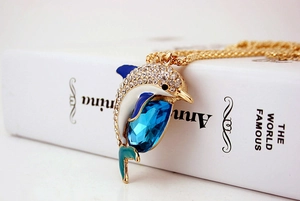 Macro detail of dolphin pendant with blue gem, crystals and teal enamel work