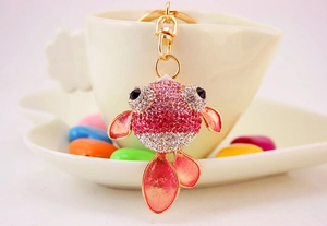 Détail d'un porte-clés poisson rose avec strass et fermoir doré suspendu sur une tasse