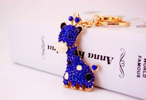Détail d'un porte-clés girafe doré avec strass bleus posé sur un livre blanc