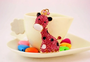 Détail du porte-clés girafe en strass roses posé à côté d'une tasse de café blanche