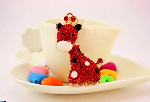 Détail d'un porte-clés girafe en strass rouges posé sur une tasse à café blanche