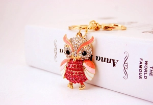 Detailed close-up of a golden owl keychain with red rhinestones and pink enamel wings