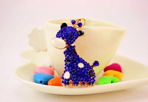 Détail d'un porte-clés girafe en strass bleus appuyé sur une tasse blanche dorée