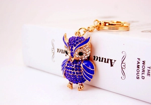 Macro detail of owl keychain with blue and white crystals on a white book background
