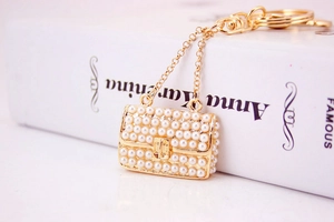 Detailed macro view of a luxury pearl-studded gold handbag keychain on a book